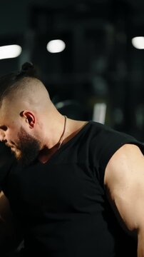 Bearded athlete with man bun grits through an intense weightlifting set in a dimly lit gym, showcasing strength, focus, and muscular effort during a challenging arm session