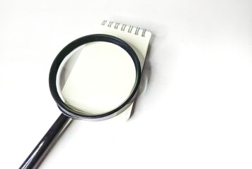 Magnifying glass and blank notebook on white background