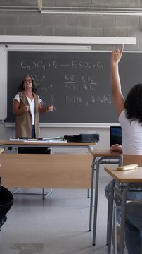 Teacher explaining chemistry lesson with students raising hands