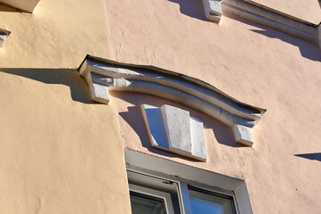 Decorative white architectural molding above window on pink and beige building facade with sharp geometric shadows cast by bright natural sunlight during the day. Decorative exterior building ornament © Tricky Shark