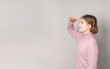 Smiling preteen girl in profile shading eyes and looking into distance on gray background with copy space.