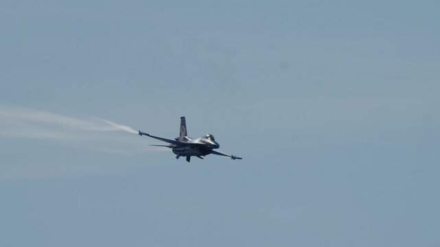 LUQA, MALTA - SEPTEMBER 28, 2025: Video footage shows a military F-16 fighter jet performing a high-speed aerobatic fly-by at an airshow, leaving vapor trails against a clear blue sky. The aircraft