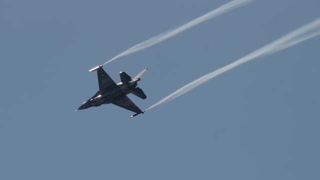 LUQA, MALTA - SEPTEMBER 28, 2025: Video footage shows a fighter jet performing a high-speed maneuver, leaving long white smoke trails against a clear blue sky. The aircraft flies away, a powerful