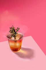 Obraz premium Smoked Old Fashioned Cocktail with Large Ice Cube and Fresh Rosemary Thyme Garnish