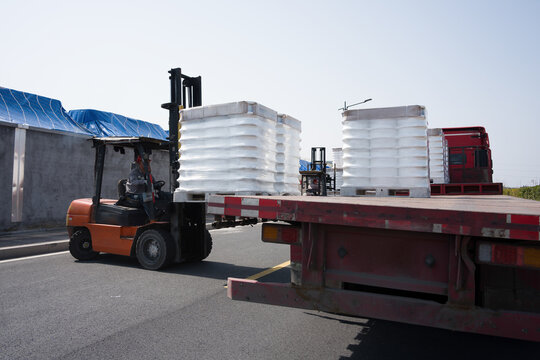 Forklift loading white bulk bags onto a flatbed truck during outdoor logistics operation