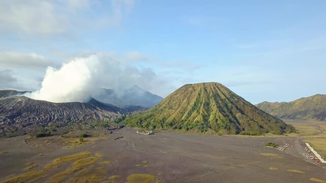 Stunning aerial view of Mount Bromo emitting white smoke alongside Mount Batok in East Java, Indonesia. Majestic volcanic landscape at Bromo Tengger Semeru National Park during a clear morning.
