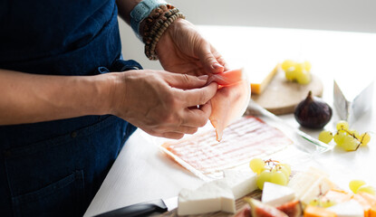 Woman Preparing A Cheese Plate In The Kitchen And Adding Ham On A Cheese Board