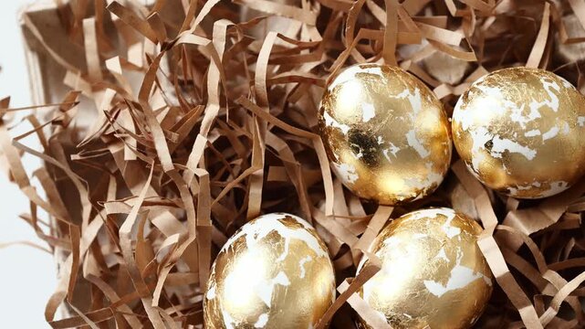 Eggs in white and gold sit on brown straw for Easter decorations.