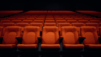 Fototapeta premium Rows of empty orange theater seats in a dark auditorium, ready for an audience
