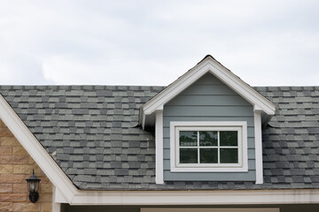 A house with a slanted roof and a window on the top. garret house with roof shingle with cloudy in rainy season. Dormer windows on the sloped shingle roof.