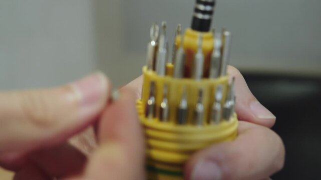 Man arranging interchangeable screwdriver bits in plastic organizer. Person placing metal bits for manual screwdriver into slots of round case. Fine motor skills development, space organization.