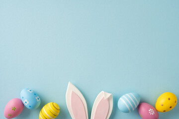 Happy Easter greeting scene with pastel painted eggs and bunny ears arranged on a soft blue...