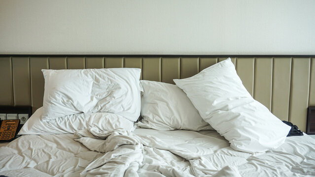 Crumpled bed sheet, a blanket and pillows after comfort duvet sleep waking up in the morning. Close-up of unfinished or messy bed. Dirty bed in hotel room.