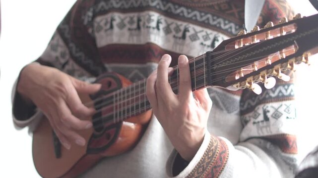 Horizontal medium shot of a musician playing the charango, a traditional small stringed instrument from the Andes. The performer is wearing a classic grey "chompa" (Andean sweater)