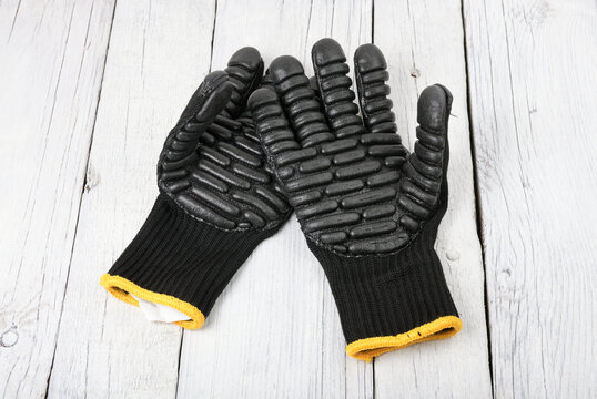 Black anti-vibration work gloves with nitrile pods on a light wooden background.