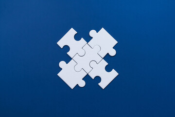 Fototapeta premium Four connected white puzzle pieces forming a square shape on blue