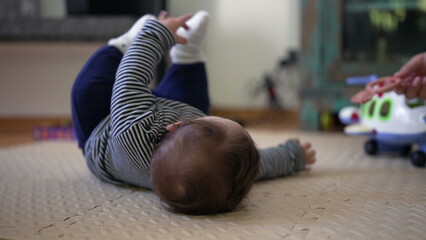 Baby lying on floor, arms raised while attempting to roll over, showcasing early developmental...