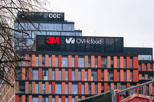 Modern commercial building with unique orange facade featuring 3M, OVHcloud, and CCC corporate logos on the roof, showcasing urban business architecture, office center infrastructure, and global compa
