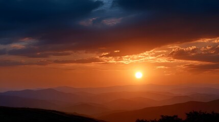 Obraz premium Dramatic sunset over layered mountain ranges with vibrant orange and yellow hues in the sky