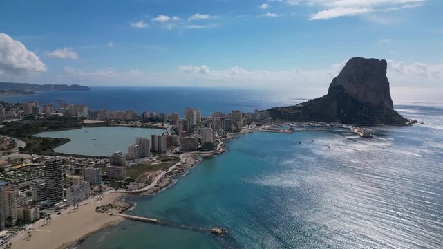 Aerial view of Calpe, a coastal city on the Costa Blanca in Spain, featuring the iconic Pe&ntilde;&oacute;n de Ifach limestone rock rising above the Mediterranean Sea.
