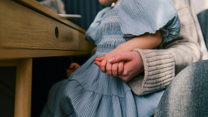Mother and child holding hands under a wooden desk, intimate moment of connection