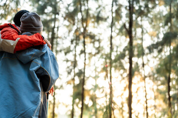 Fototapeta premium Couple Hugging in Forest at Sunset. Rear View of Romantic Travelers in Warm Winter Clothes Standing Together, Embracing Peacefully While Enjoying the Tranquil Nature and Soft Golden Light