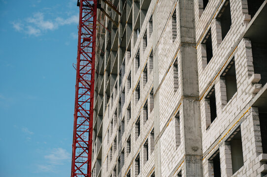 Construction site with concrete building and red crane against blue sky