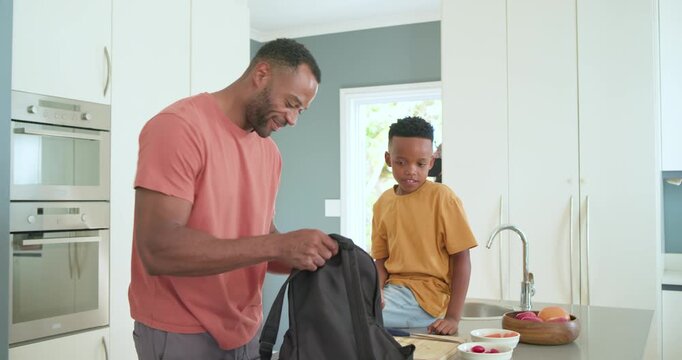 African American father and son with father handing apple, zipping black backpack, leaving kitchen