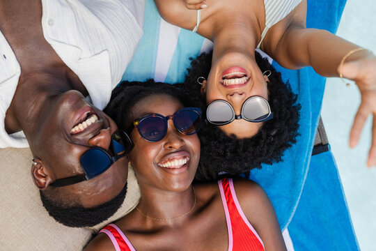Three pairs of sunglasses are reflecting bright sun on blue-and-white towel beside pale pool water