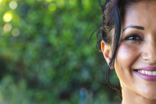 Adult woman smiling, showing mauve lipstick and eyeliner in garden with ear stud, copy space