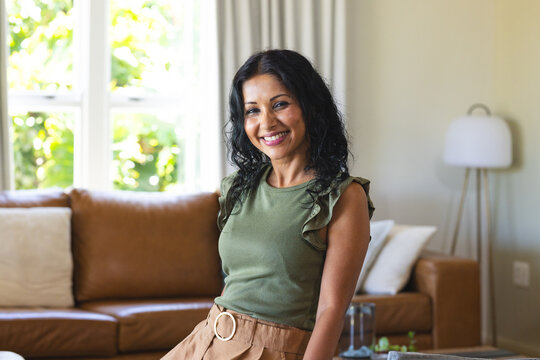 Indian woman sitting on brown leather couch, smiling, wearing olive-green top and tan skirt