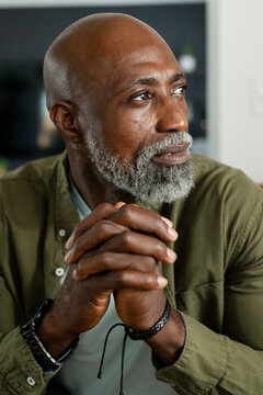 Senior African man sitting home clasping, looking thoughtful, wearing olive shirt, watch, bracelet