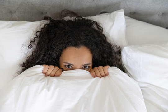 Person is lying in bed while duvet is covering face, hands gripping edge against tufted headboard