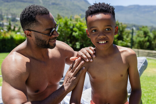 African American shirtless father and son standing on lawn placing hand on son's shoulder