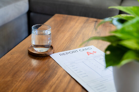 Glass resting on coaster on wooden table while report card showing letter A+ lying near plant