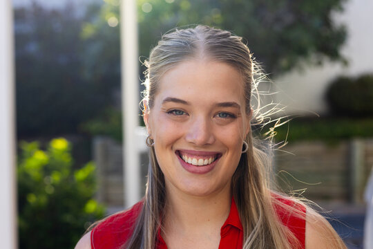 Woman smiling while posing on residential patio, showcasing sleeveless red top and hoop earrings