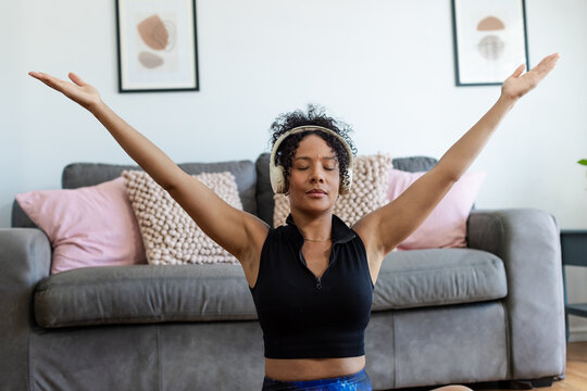 African American woman sitting on floor in living room, stretching in sportswear with headphones