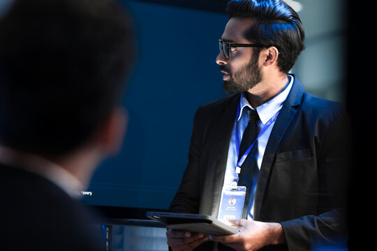 An Indian male software engineer or team lead discusses Python code for an AI algorithm. A developer in the audience raises their hand to ask a technical question during a code review.