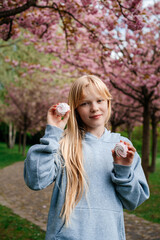 Fototapeta premium Blonde girl holding pink meringue cookies under cherry blossoms