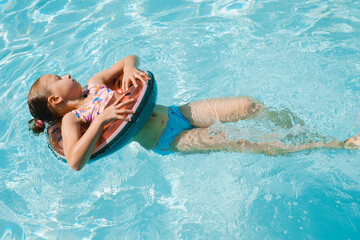 Top view of happy child floating on watermelon inflatable ring in swimming pool. Kid relaxing in blue water on summer vacation resort.