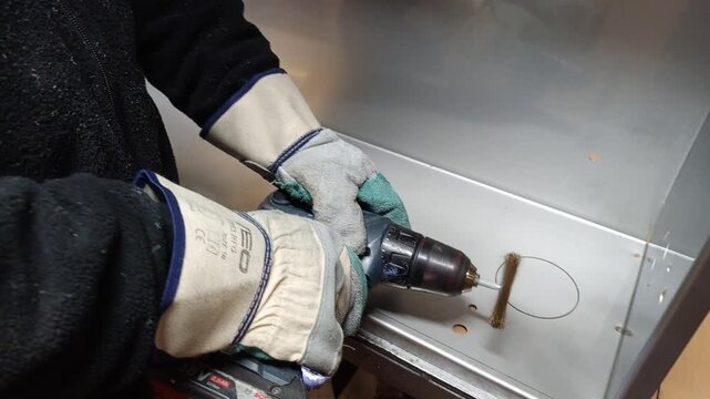 Cleaning welding residues on metal cabinet corners using a wire brush drill attachment.