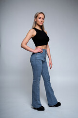 Female Fashion Model Posing in Stylish Outfit with Flared Pants and Crop Top Against Neutral Background