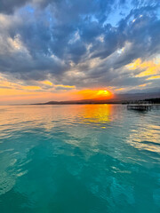 Fototapeta premium Turquoise water of Issyk Kul at sunset with golden reflection and dramatic clouds.