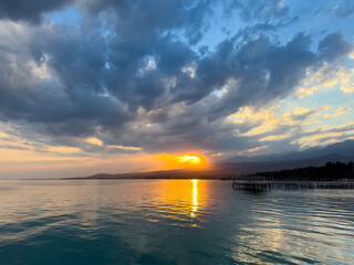 Obraz premium Sunset at Issyk Kul Lake in Kyrgyzstan. Bright sun breaking through clouds reflecting in clear turquoise water.