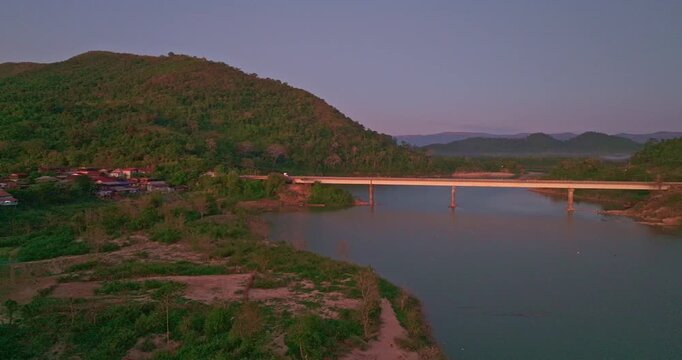 Scenic panorama capturing the tranquil flow of the Nam Kading River beneath a glowing sunset sky, highlighting natural beauty and local infrastructure.