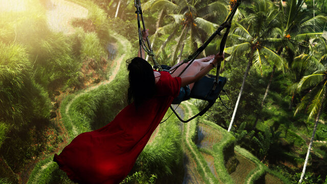 bali swing red dress Bali Swing Trend. Caucasian Woman in Long Red Dress Swinging in the Jungle Rainforest. Vacation in Asia. Travel Lifestyle Stock Photo