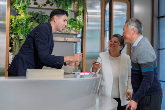 Friendly concierge assisting senior couple at modern hotel reception desk, providing direction with warm service and welcoming hospitality in a stylish urban environment.