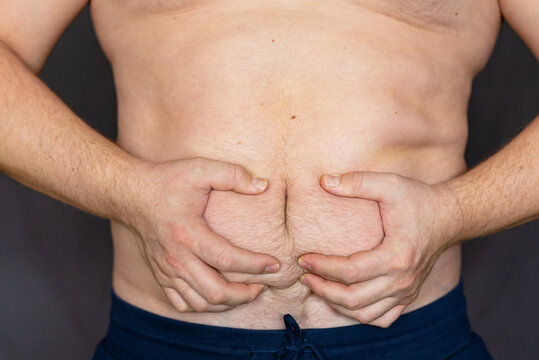 Shirtless man squeezing abdominal fat on dark background