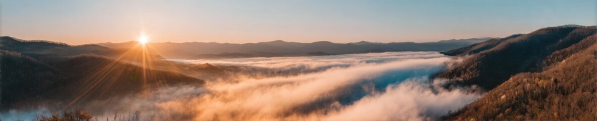 Naklejka premium Panoramic mountain landscape at sunrise with thick white clouds filling the valley below, vibrant golden sunlight lens flare and blue sky over wilderness peaks at dawn