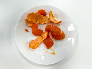 Orange peel on a white pate seen from above, leftover from eating the fruit as a snack.